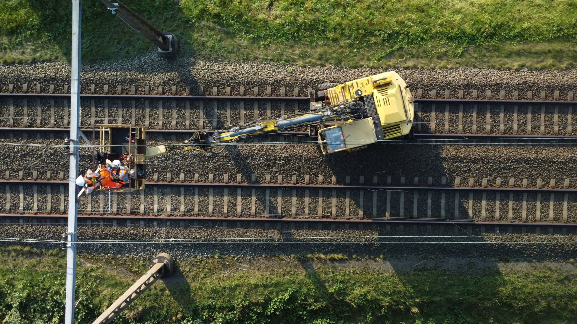 Luchtfoto van een spoorwerkplek: een hoogwerker op het spoor met twee monteurs bij een bovenleidingmast