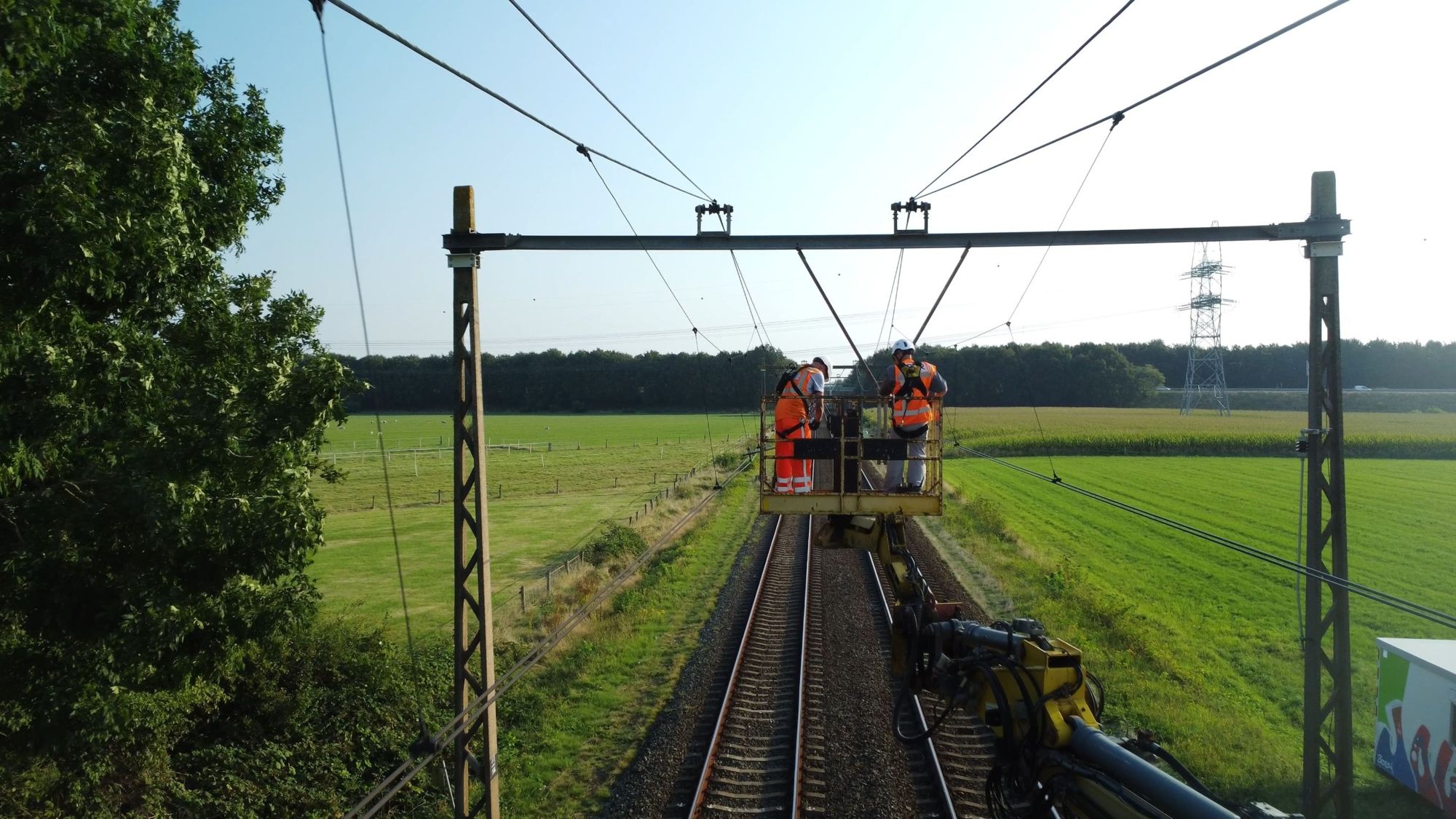 Twee monteurs in een hoogwerker werken aan de bovenleiding boven een dubbel spoor